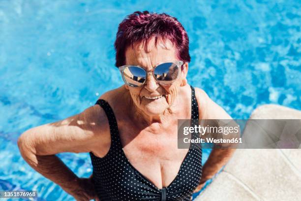 senior woman wearing sunglasses while making a face in pool - alte frau badeanzug stock-fotos und bilder