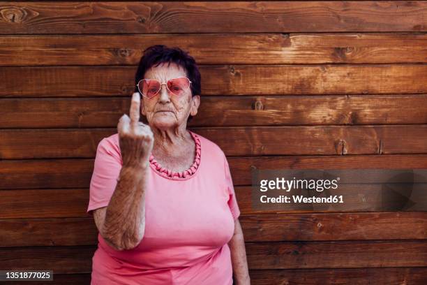 senior woman gesturing in front of wooden wall - doigt dhonneur stock pictures, royalty-free photos & images