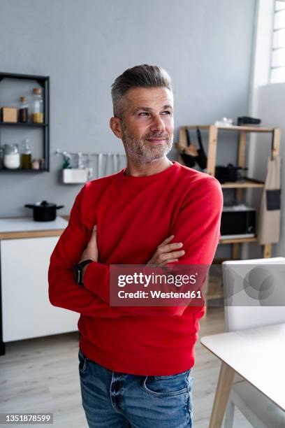 thoughtful mature man standing with arms crossed in kitchen - red jumper stock pictures, royalty-free photos & images