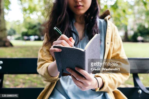 young woman writing in diary at park - diário imagens e fotografias de stock