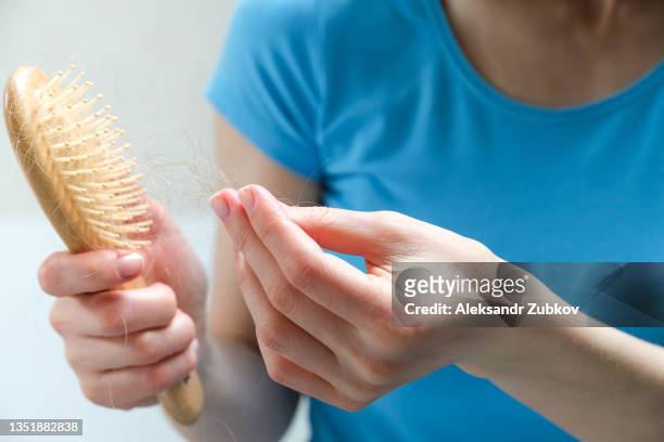 a woman holds a wooden comb in her hands, cleans it of fallen hair after combing. the concept of head health problems, deficient conditions in the body due to stress and depression, a consequence of chemotherapy and radiation for cancer. - hairbrush 個照片及圖片檔