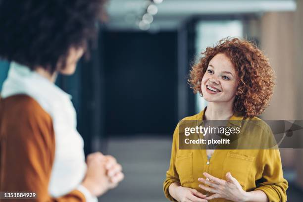 jeune femme rousse souriante parlant à un collègue au bureau - business talk petite phrase photos et images de collection