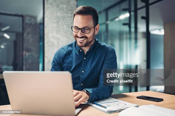 smiling businessman using laptop in the office - candid office stockfoto's en -beelden
