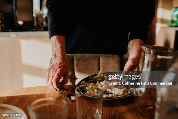 a man lifts a plate of leftover food from a wooden table - picky eater stock pictures, royalty-free photos & images