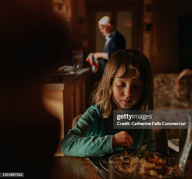 a young girl sits at a kitchen table and eats her dinner. scene is tranquil and calm. - picky eater stock pictures, royalty-free photos & images