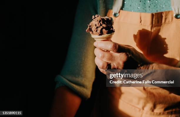 close-up of a woman putting chocolate ice-cream in a small wafer cone - chocolate ice cream cone stock pictures, royalty-free photos & images