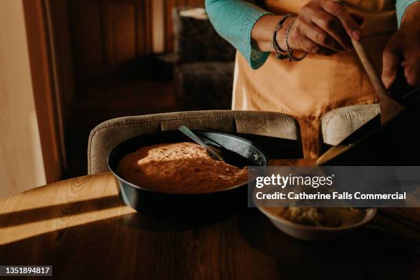 woman pours custard from a saucepan onto a piece of sponge cake in a bowl - custard fotografías e imágenes de stock