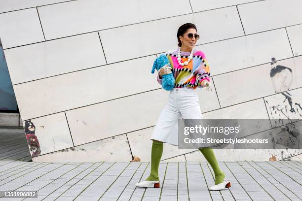 Influencer Salome Chaboki, wearing a multicolor mohair-blend knit sweater by Essential Antwerp, white bermuda shorts by Acne Studios, a blue faux fur...