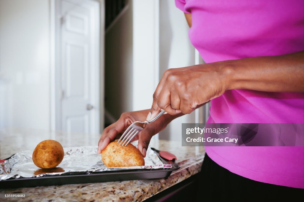 Woman Pierces Raw Potato With Fork Before Baking