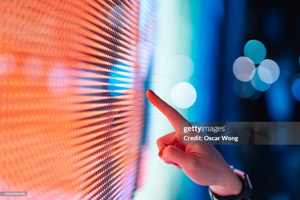Close-up of female hand touching illuminated digital display in the dark.
