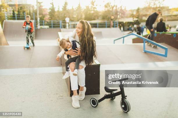 beautiful mother and daughter sitting at skate park together smiling happily - mother and daughter riding on skateboard in park stock pictures, royalty-free photos & images