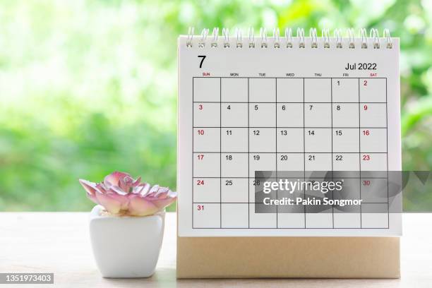 calendar desk 2022 on july month, calendar planning and houseplant on wooden table with green tree nature background. - calendar pages stock pictures, royalty-free photos & images