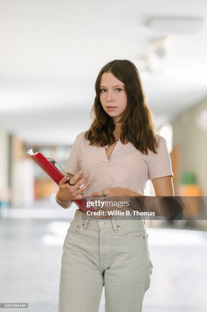 High School Student In Corridor Holding Notepad