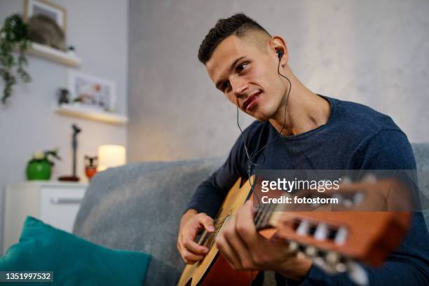 smiling young man practicing playing a song on acoustic guitar - muzieksymbool stockfoto's en -beelden