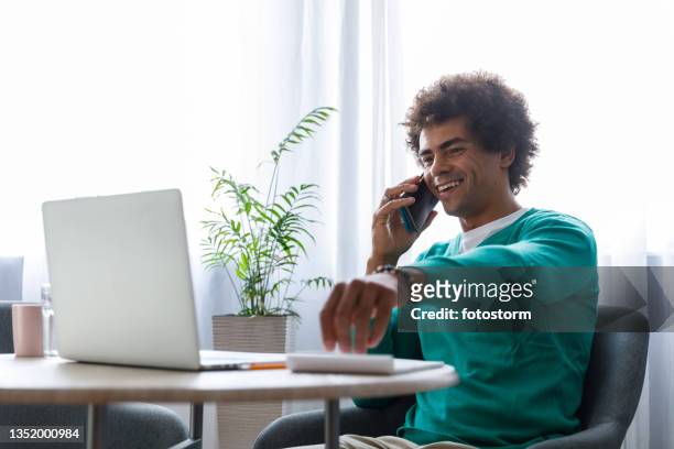 fröhlicher junger mann bei einer telefonkonferenz, der nach einem bleistift greift, um notizen zu machen - aquamarin stock-fotos und bilder