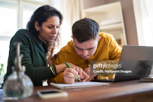 young man with down syndrome with his tutor studying and using laptop indoors at home, homeschooling. - disability computer stock pictures, royalty-free photos & images