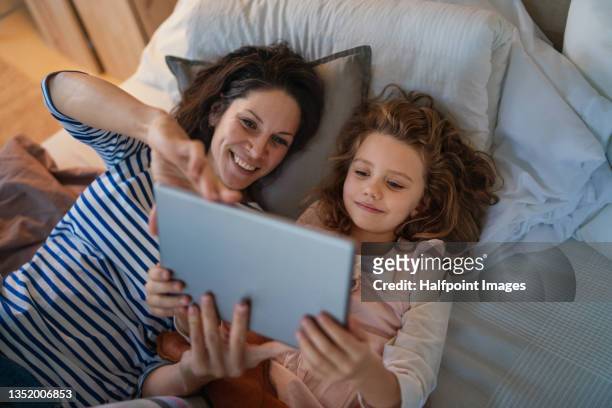 high angle view of little girl with her mother lying on bed holding tablet at home. - child and ipad stockfoto's en -beelden