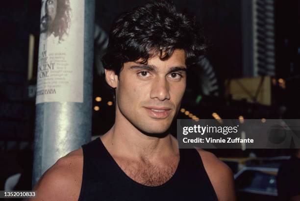 Cuban-born American actor Steven Bauer, wearing a black vest, circa 1985. A Meher Baba flyer on the lamppost behind Bauer reads 'I am the ancient...