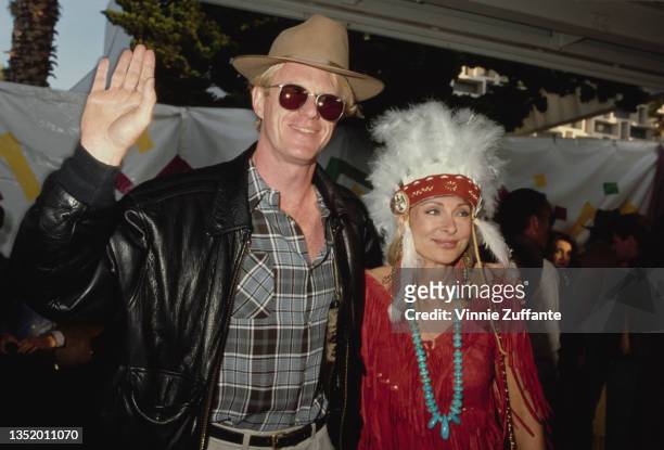 American actor Ed Begley Jr wearing a grey, black and white plaid shirt beneath a black leather jacket, with sunglasses and a fedora, with a woman...
