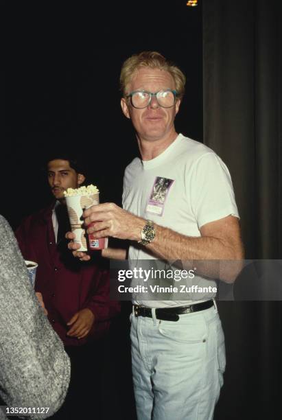 American actor Ed Begley Jr carrying a tub of popcorn and a disposable cup of Pepsi, wearing a white t-shirt on which is attached a 'Darryl Hall and...