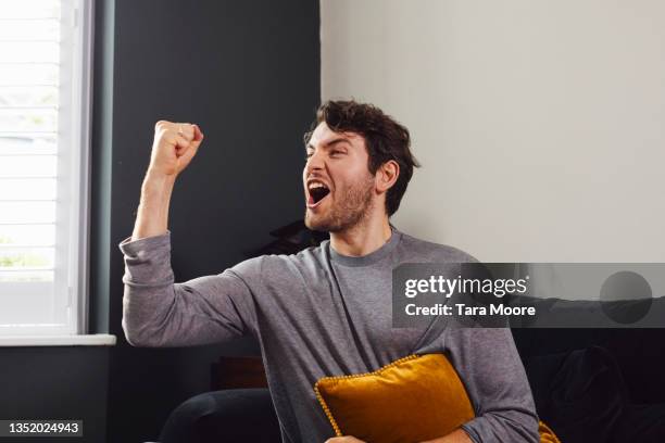 young man sitting on sofa. - faust in die luft stoßen stock-fotos und bilder