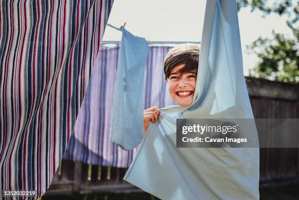 happy boy hiding behind clothes hanging on a clothesline outside. - draped sheet stock pictures, royalty-free photos & images