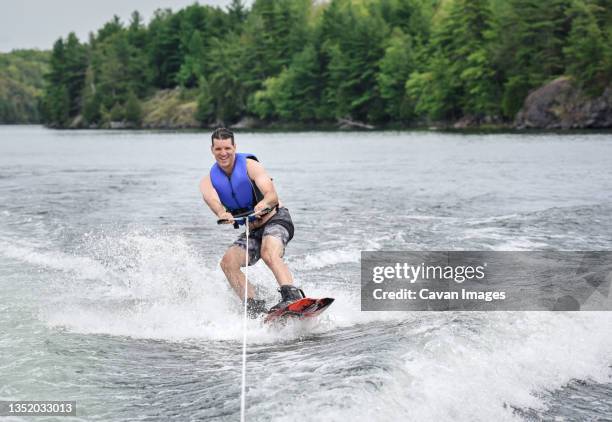 man wake boarding while being pulled by a boat on a lake. - waterskiing stock pictures, royalty-free photos & images