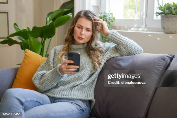 attractive middle aged woman sitting on the couch (negative emotions, smartphone)) - tech problems stock pictures, royalty-free photos & images