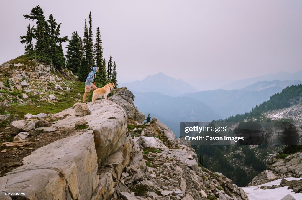 Male hiker and fluffy dog standing on cliff in the alpine