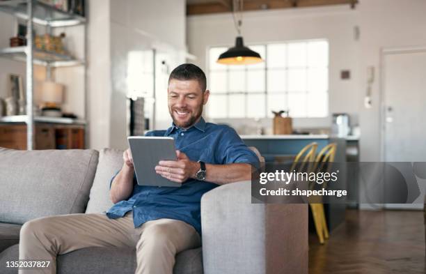 shot of a handsome man relaxing on his sofa using a digital tablet - bachelor apartment stock pictures, royalty-free photos & images