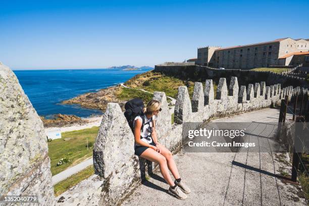 pilgrim woman sitting on the wall of a castle against the sea - bayonne imagens e fotografias de stock