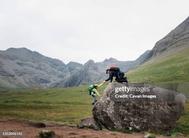 father helping son climb a rock in isle of skye, scotland - highlands schottland wandern stock-fotos und bilder