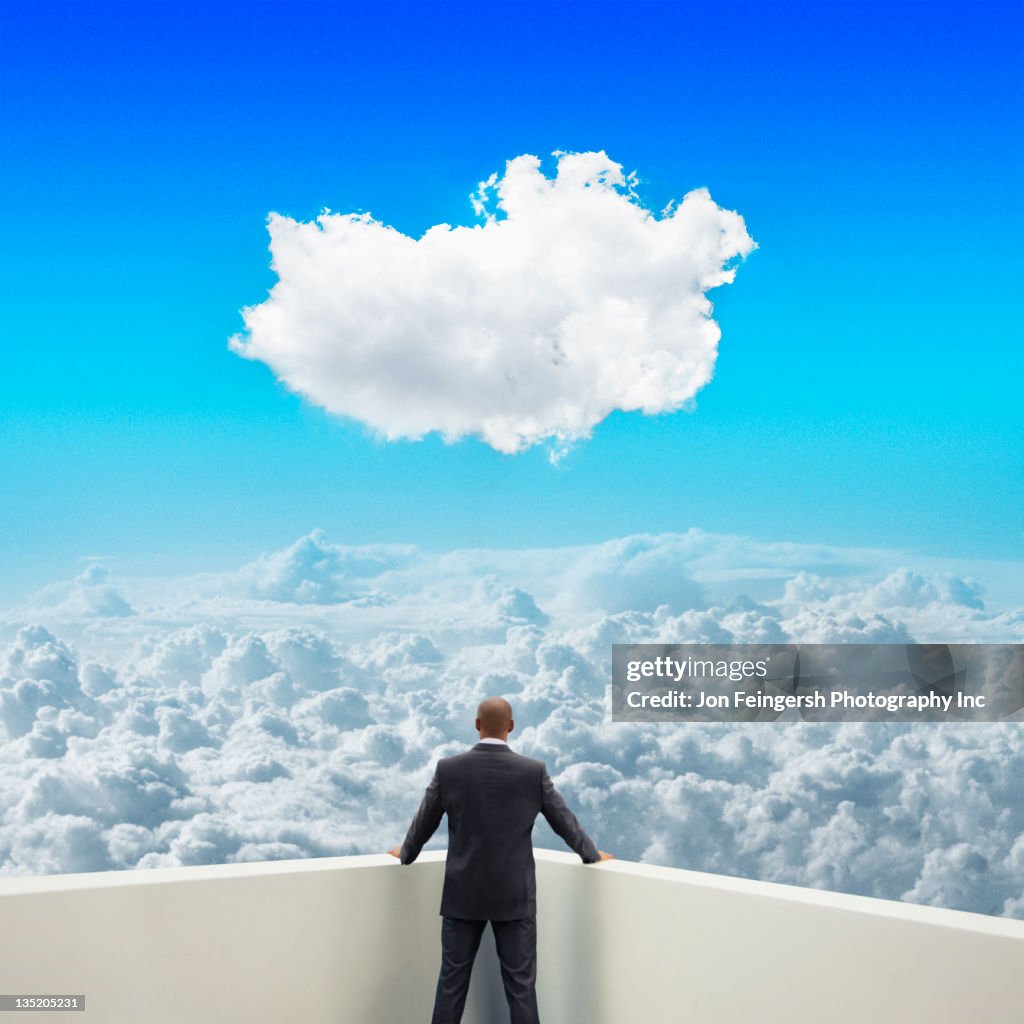 Black businessman on balcony looking at clouds