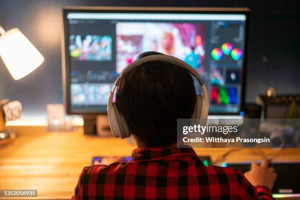 man doing video editing on computer with headphones - deitando fotografías e imágenes de stock