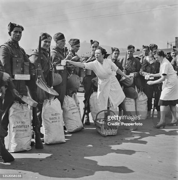 Members of the Women's Voluntary Service distribute cups of tea and cakes to British Army soldiers arriving at an English port prior to embarking on...