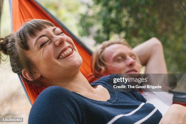 young woman laughing while lying next to boyfriend in hammock - risa fotografías e imágenes de stock