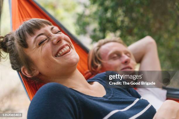 young woman laughing while lying next to boyfriend in hammock - woman hammock photos et images de collection