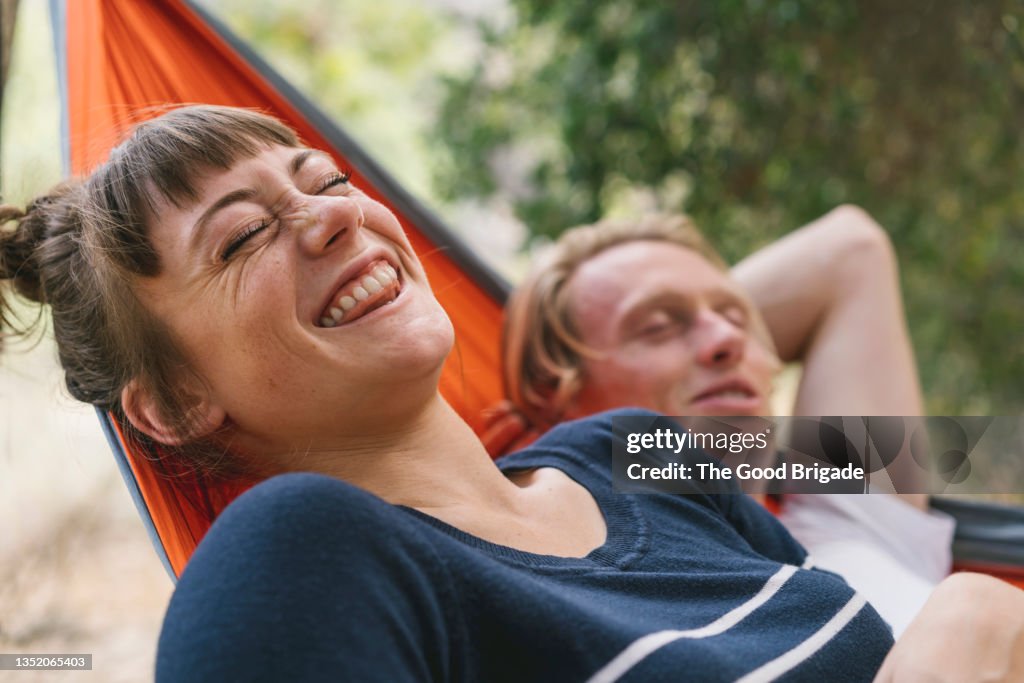 Young woman laughing while lying next to boyfriend in hammock