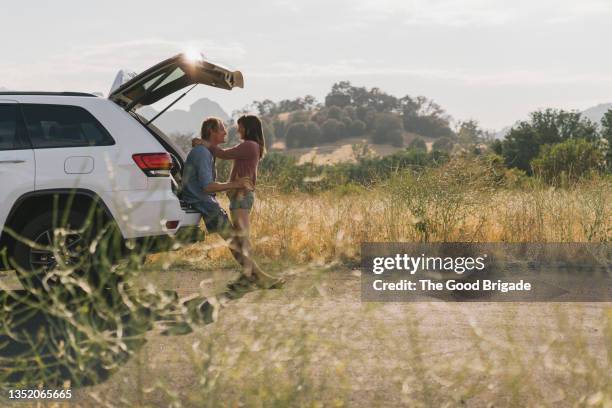 couple embracing at back of car on road trip - couple with car stock-fotos und bilder