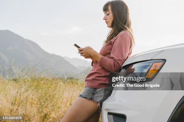 young woman using smart phone while leaning on car - leaning stock pictures, royalty-free photos & images