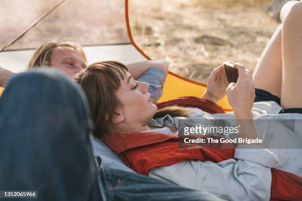 girlfriend using smart phone while leaning on boyfriend in tent - mid volwassen mannen stockfoto's en -beelden
