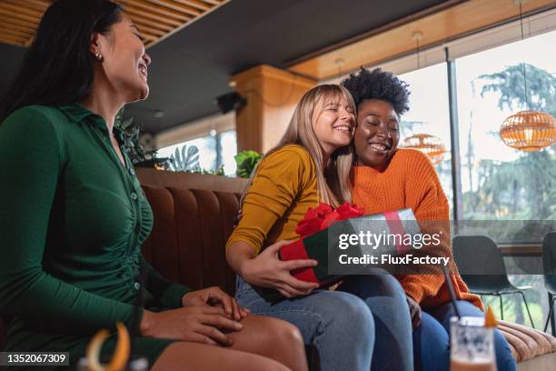 lovely woman, expressing her gratitude, after her multiracial female friends surprised her with a gift - birthday gift stock pictures, royalty-free photos & images