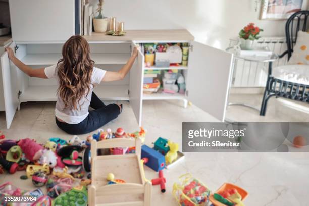 a woman is organizing her daughter's toys in the living room - arranjo imagens e fotografias de stock