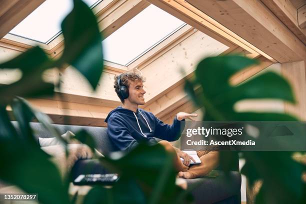 young man relaxes in brightly lit, modern apartment - skylight stock pictures, royalty-free photos & images