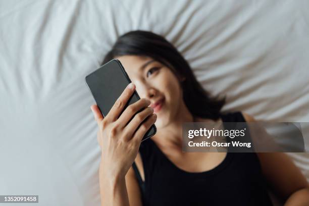 high angle view of young woman using smart phone on bed - dating app stock pictures, royalty-free photos & images