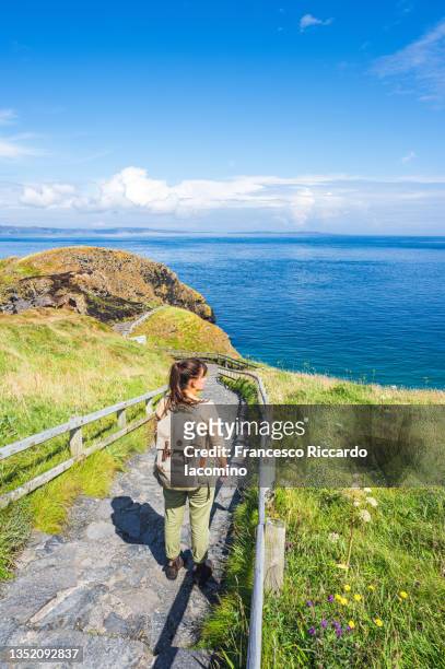 uk, northern ireland, county antrim, ballintoy, woman walking on the path to carrick-a-rede rope bridge, - ireland travel stock pictures, royalty-free photos & images