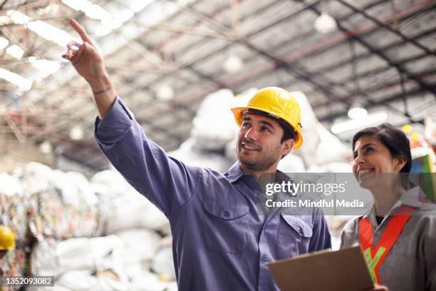 smiling male blue-collar recycling worker pointing up while talking with coordinator - waste management stock pictures, royalty-free photos & images