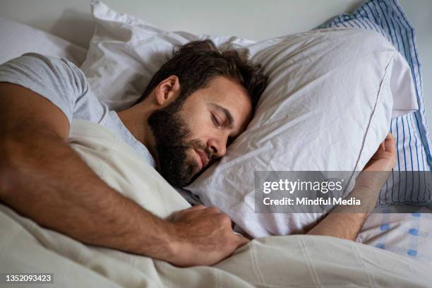 young adult man lying in bed while sleeping - travesseiro imagens e fotografias de stock