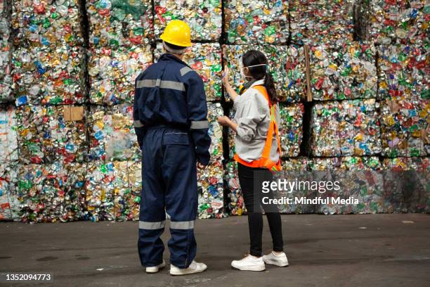 männliche und weibliche abfallwirtschaftsarbeiter stehen vor stapeln von verdichteten wertstoffen - wiederverwertungsanlage stock-fotos und bilder
