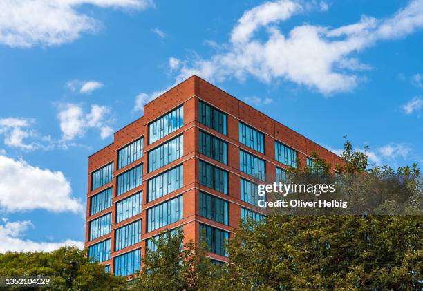 exterior low angle view of a modern office building with a facade of red brick works and large windows. in the foreground lot of trees - office brick exterior stock pictures, royalty-free photos & images